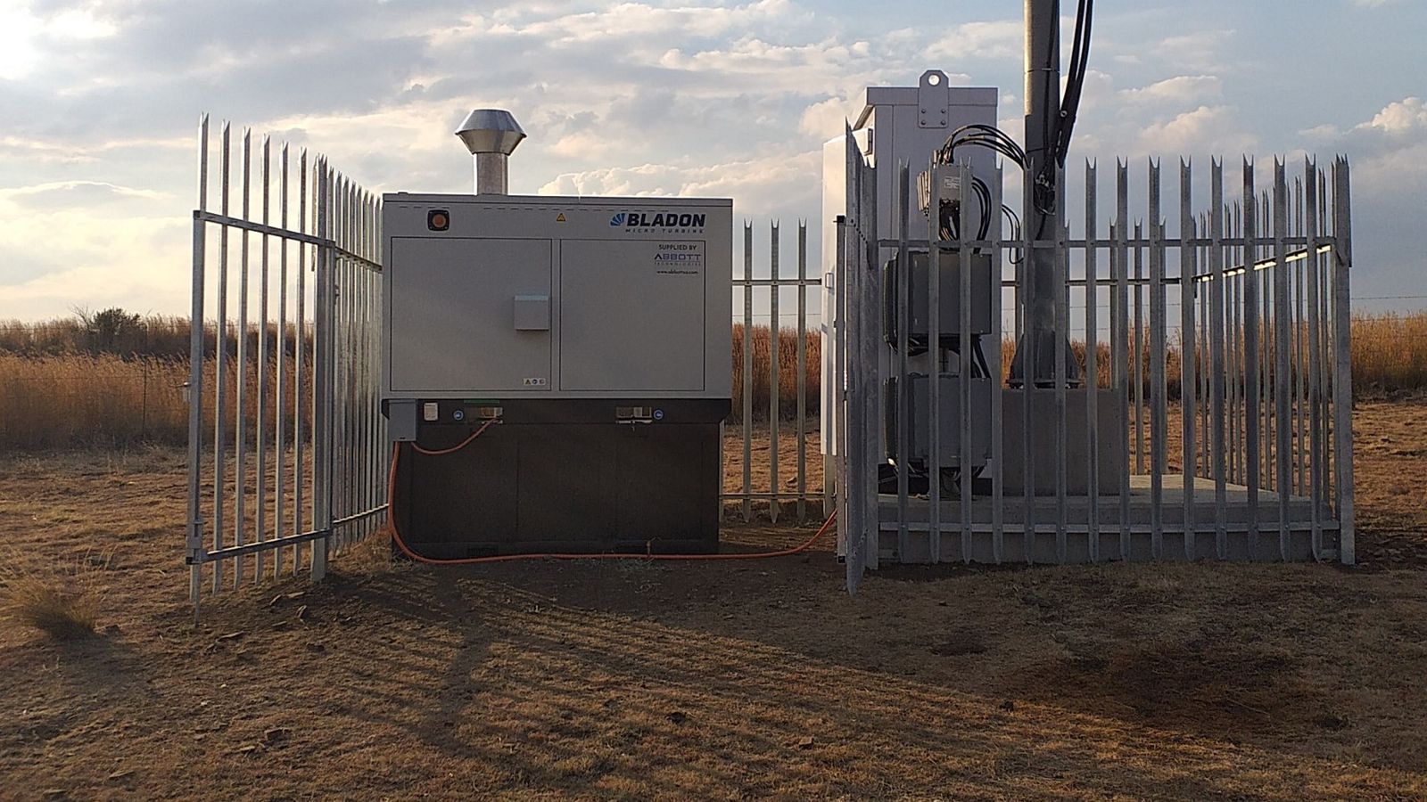 Bladon microturbine genset behind a palisade security fence at a rural off grid telecom tower site in West Africa